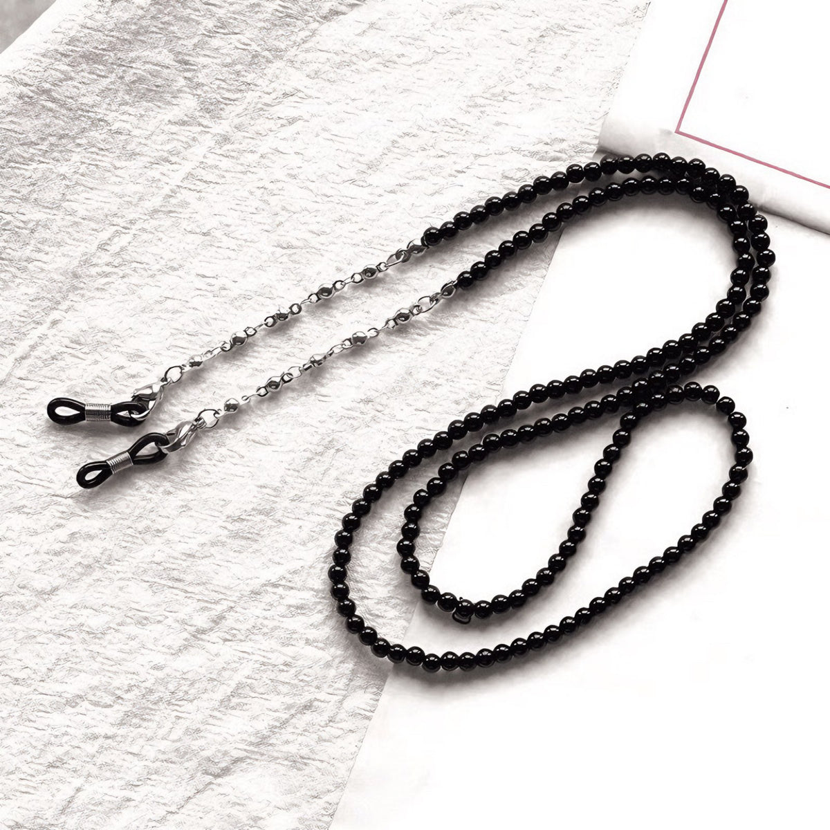 Black beaded eyeglass chain with silver-tone links and adjustable end loops, flat lay