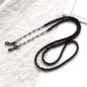 Black beaded eyeglass chain with silver-tone links and adjustable end loops, flat lay