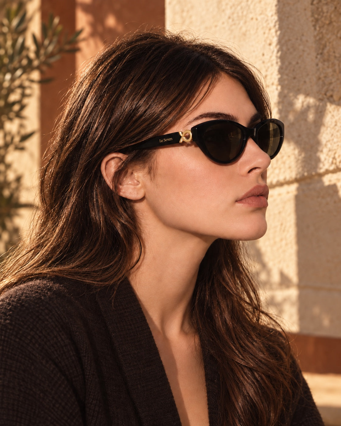 Model wearing Mira Black sunglasses in warm sunlight, with the gold Le Seven mark behind the sculpted temple accent